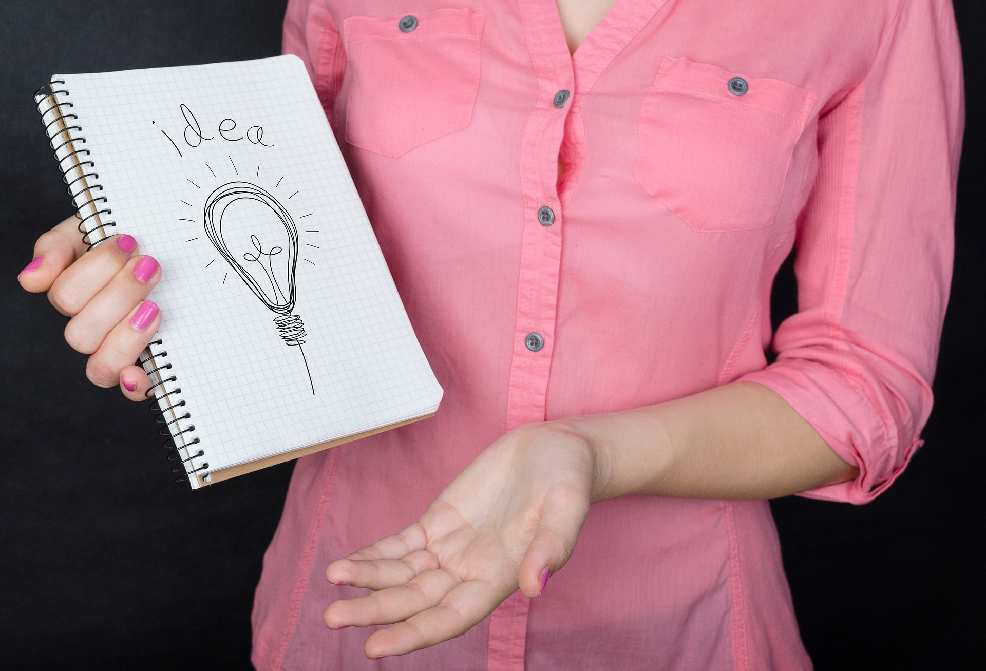 Na zdjęciu fragment kobiecej postaci trzymającej w dłoni notes z napisem Idea.