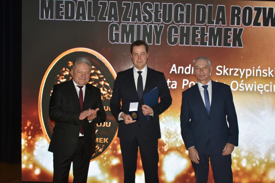 Starosta prezentuje medal otrzymany z rąk widocznego na scenie obok burmistrza Chełmka oraz przewodniczącego rady miejskiej