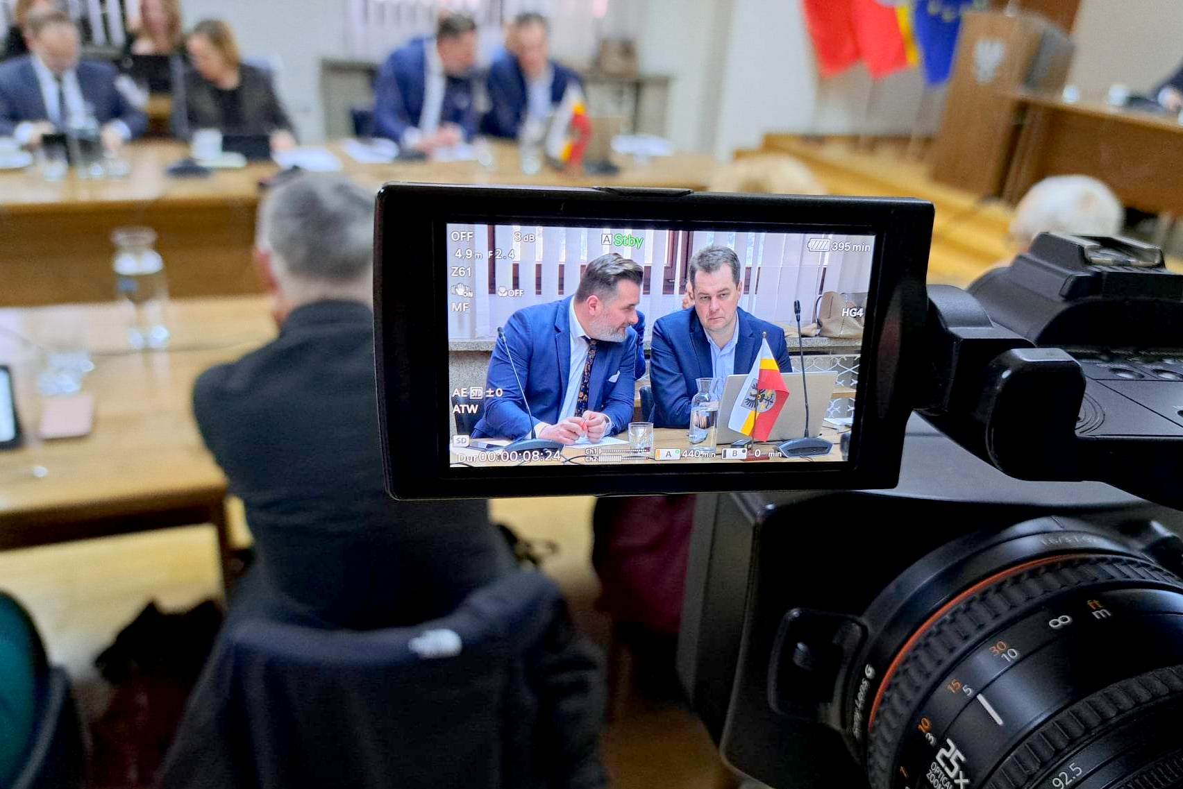 Na ekranie kamery widać rozmawiających ze sobą na sesji rady powiatu starostę i wicestarostę