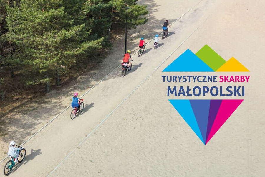Widok z góry na jadącą dołem grupę rowerzystów, a w prawym górnym roku napis Turystyczne Skarby Małopolski