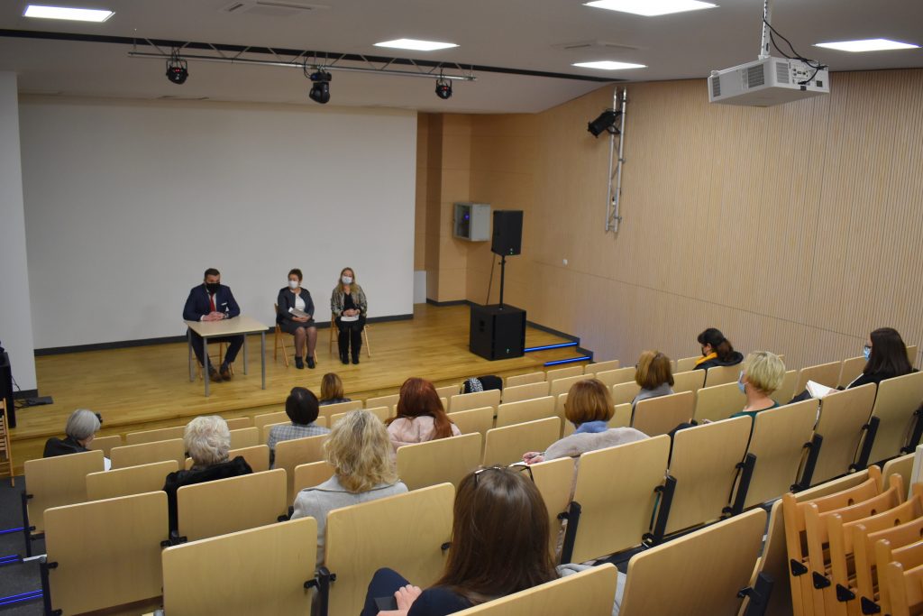Aula trzy osoby na scenie kilka osób siedzi na widowni.