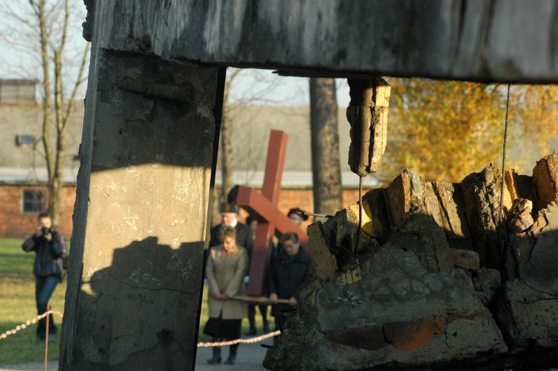 Ruiny jednego z krematoriów w Birkenau, w tle majączący się duży drewniany krzyż niosący przez wiernych
