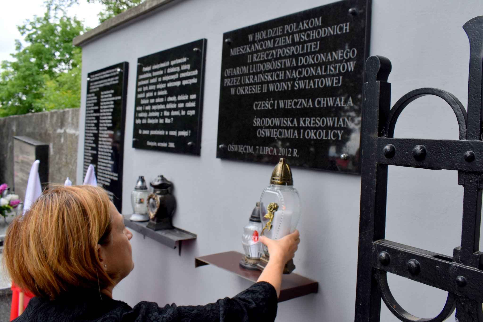 Członkini zarządu powiatu Teresa Jankowska kładzie znicz pod tablicą upamiętniającą ofiary zbrodni ukraińskich nacjonalistów.