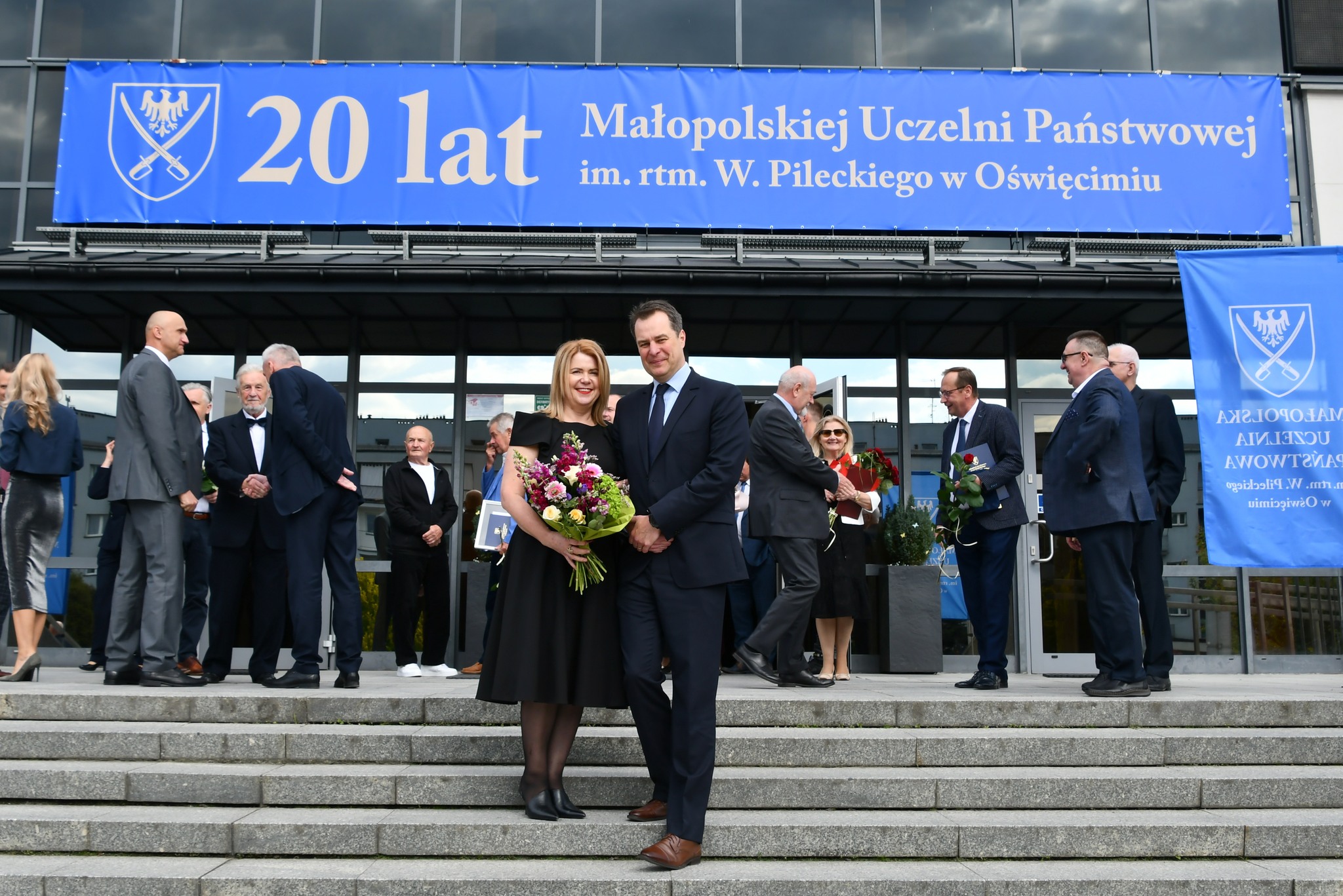 Na schodach OCK pod banerem z napisem 20 lat uczelni pozują do pamiątkowego zdjęcia pani rektor i pan starosta
