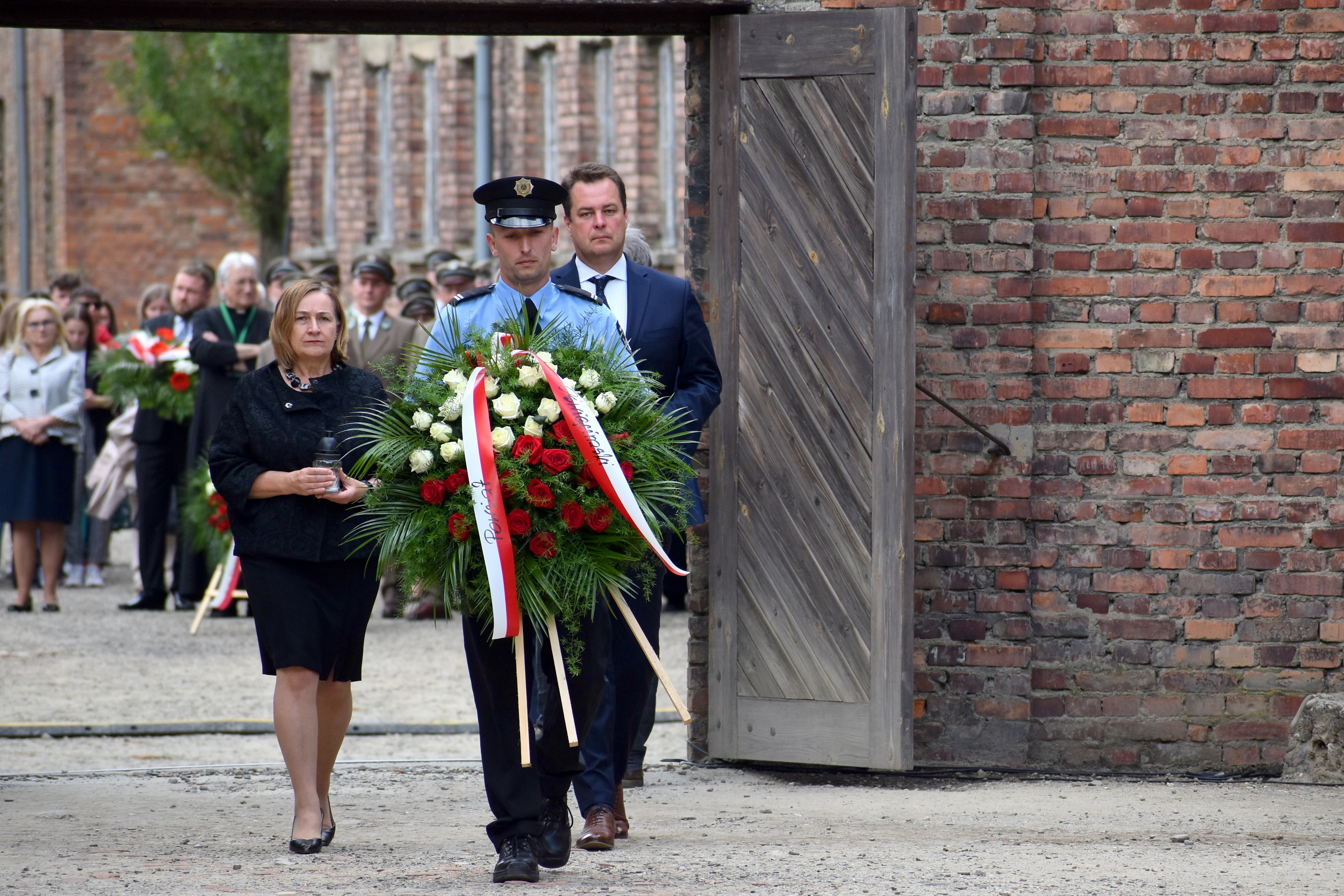 Na zdjęciu strażnik muzealny niosący wieniec, a za nim podążający w stronę Ściany Śmierci starosta i członkini zarządu powiatu.