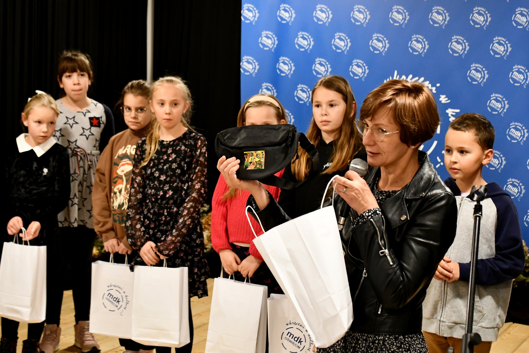 Dyrektorka MDK na tle laureatów prezentuje torbę z naniesionym obrazkiem
