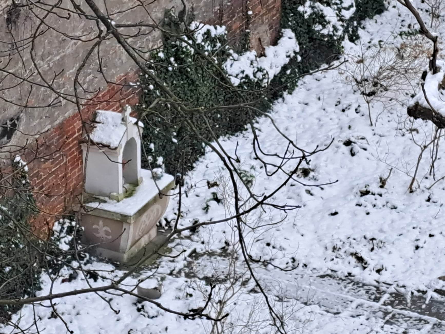Widok z okna na zaśnieżony dziedziniec, na którego lewej ścianie stoi niepozorna biała kapliczka
