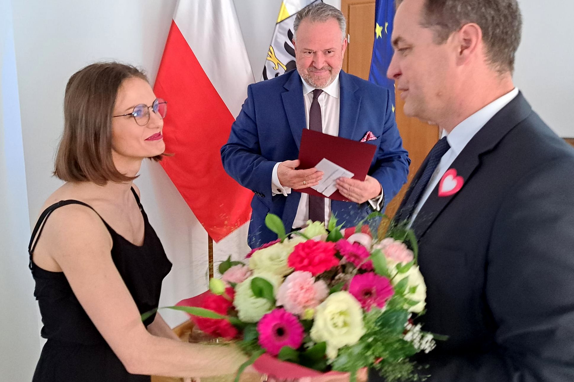 Starosta wręcza kwiaty mistrzyni świata w brydżu. W tle widać sylwetkę przewodniczącego rady powiatu