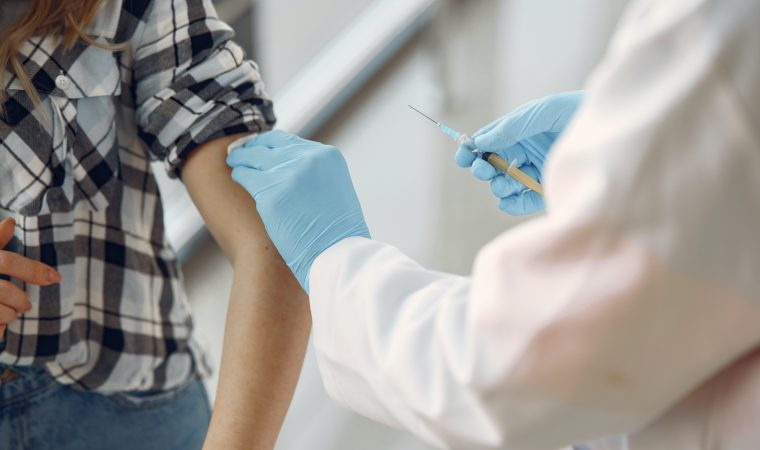 Lekarz dezynfekujący miejsce szczepienia na ręce osoby. Trzyma w ręce szczepionkę