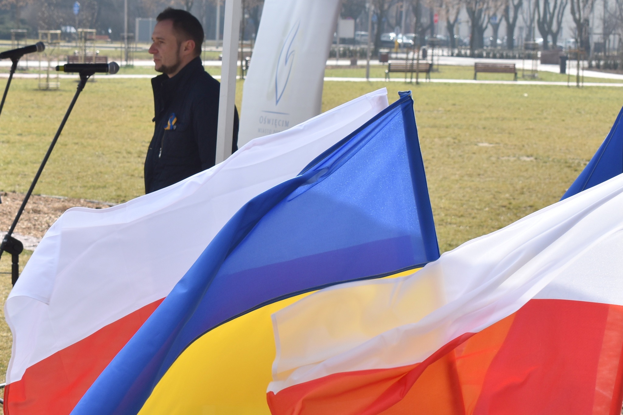 Przemawia Ukrainiec Artem Bogucki. Na pierwszym tle flagi polskie i ukraińskie