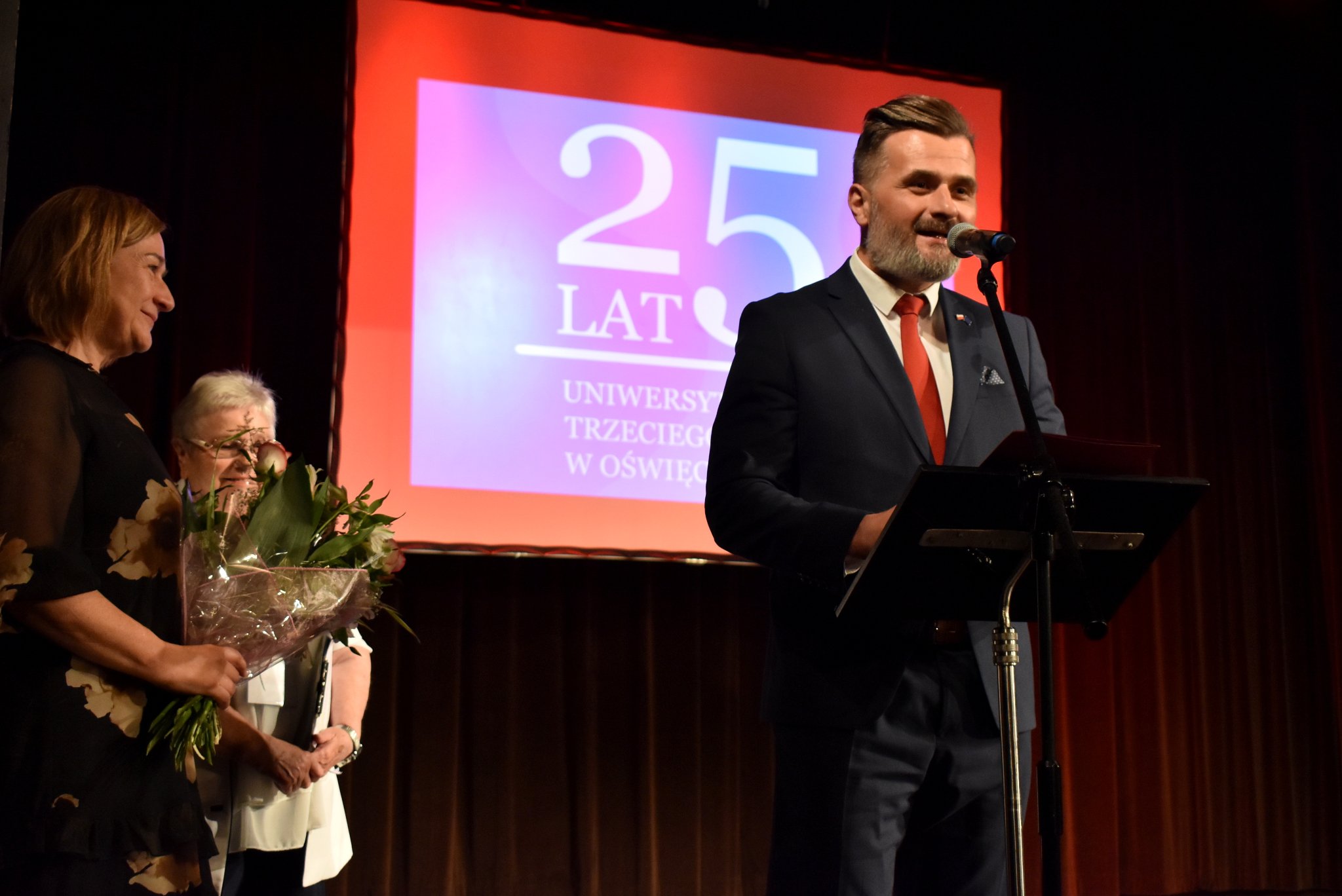 Wicestarosta Paweł Kobielusz składa gratulacje stojącej obok na scenie OCK Karolinie Domider z UTW. Obok stoi Teresa Jankowska, członkini zarządu powiatu.