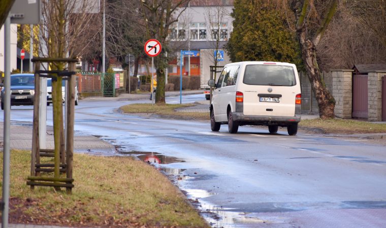 Zdjęcie drogi, pośrodku niej jedzie biały samochód.