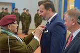 Starszy mężczyzna w mundurze po lewej stronie wręcza medal mężczyźnie po prawej stronie
