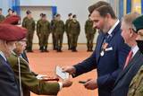 Starszy mężczyzna w mundurze po lewej stronie wręcza medal mężczyźnie po prawej stronie