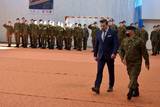 Osoby w mundurach wojskowych stoją po lewej stronie. Po prawej stronie idzie osoba w garniturze i druga osoba w mundurze wojskowym