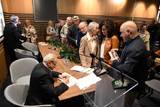 Siedzący za stołem w Muzeum Pamięci Tadeusz Firczyk wpisuje się chętnym do egzemplarzy albumu swojego autorstwa.