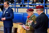 Po lewej stronie mężczyzna w garniturze, a po prawej stronie osoby w mundurach wojskowych